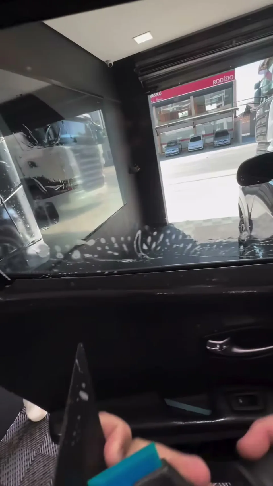 Vista de dentro do carro pelo vidro da porta, com a rua ao fundo, no estúdio da Black Films