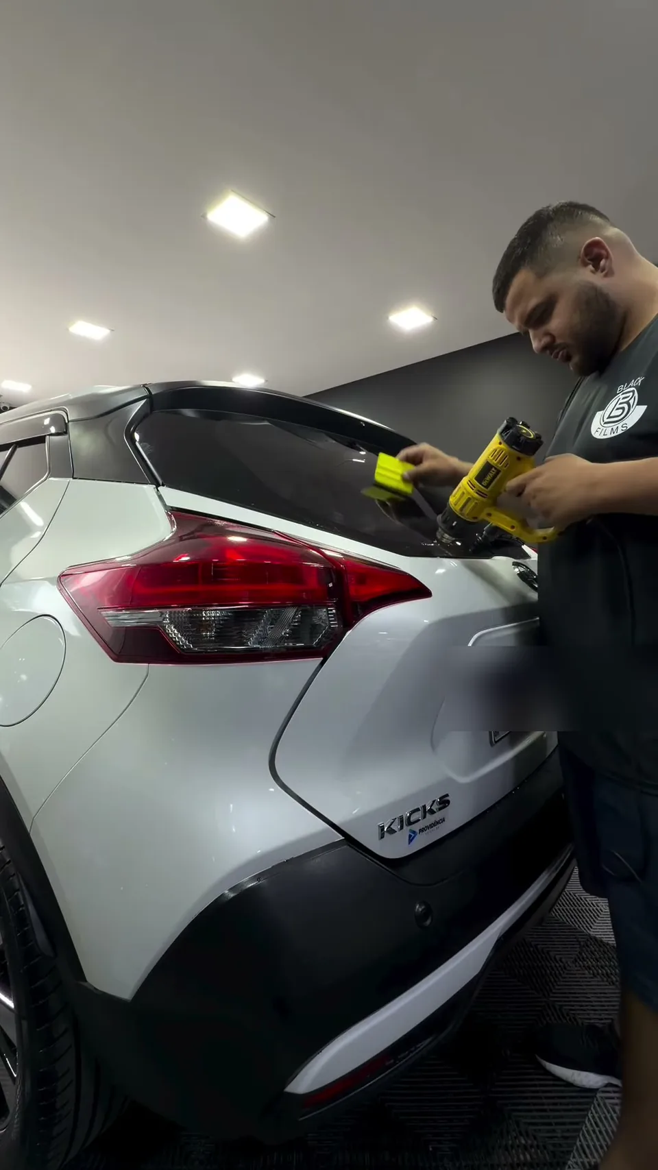 Técnico da Black Films aplicando película no vidro de um Nissan Kicks branco